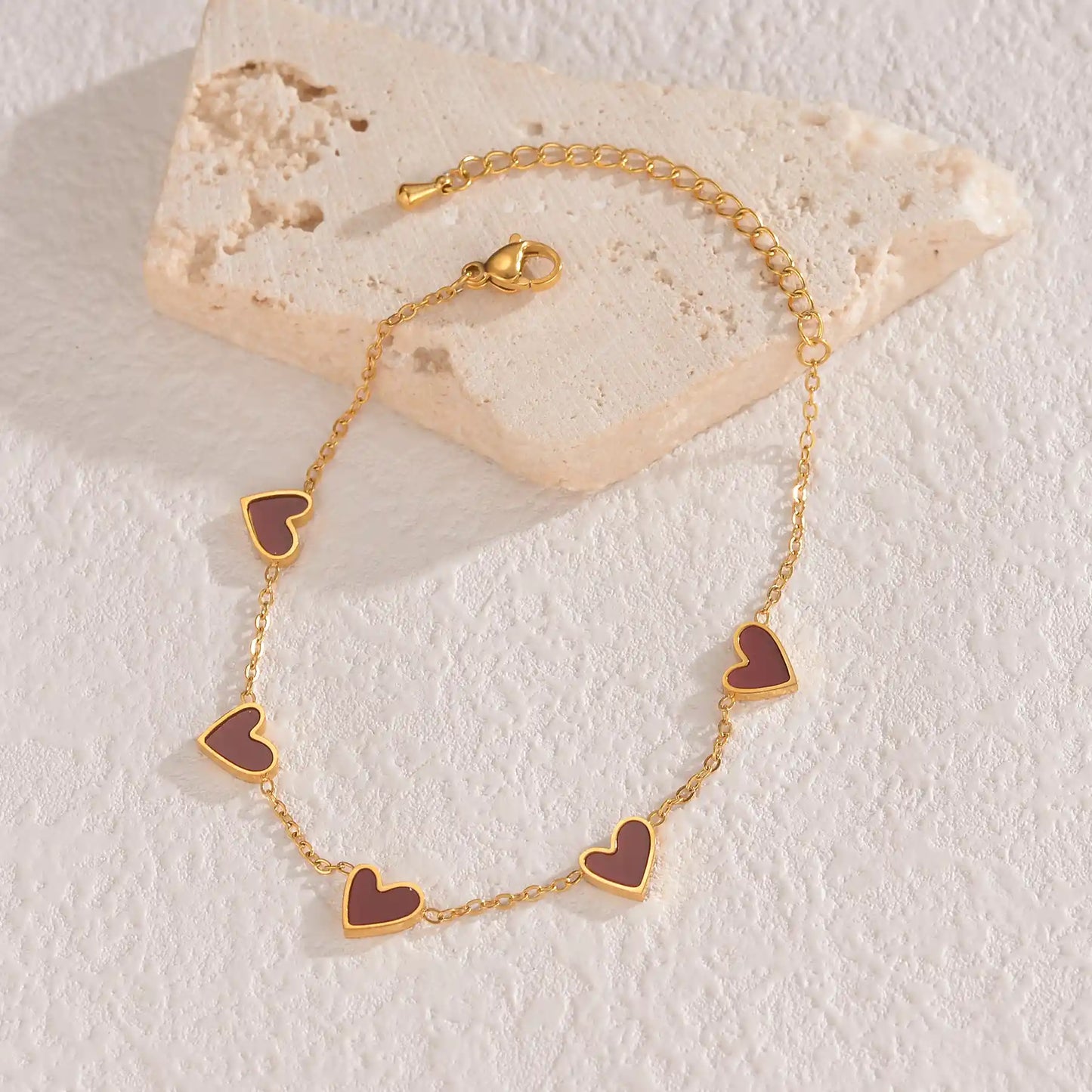 Gold bracelet with heart-shaped charms on a light stone surface